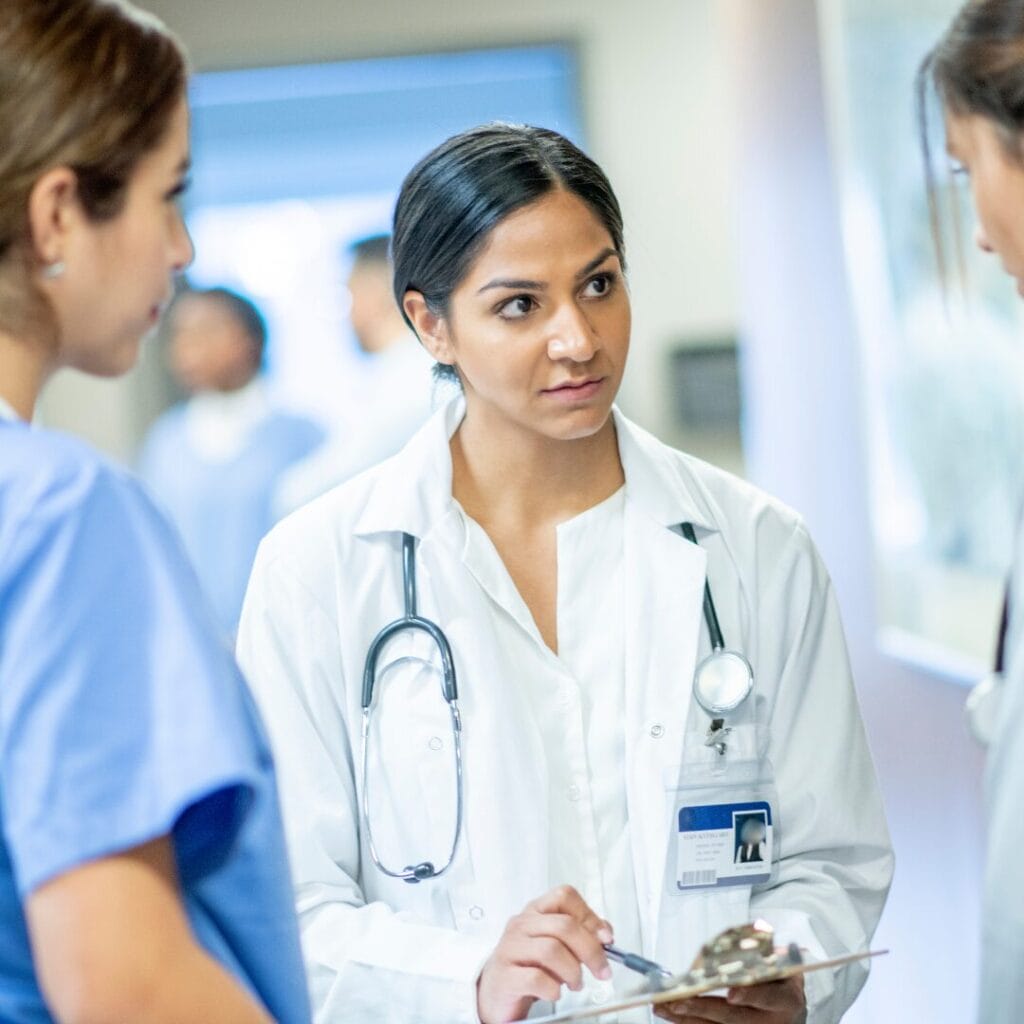 A doctor talks to other doctors in the hallway of a hospital